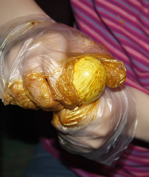 Los huevos brillantes de Pascua de colores en las manos con guantes durante el proceso de coloración
 - Foto, Imagen