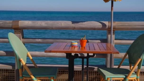 Cozy beach cafe with beautiful view on the sea. Wooden table and chairs prepared for clients by the sea coast. - Metraje, vídeo