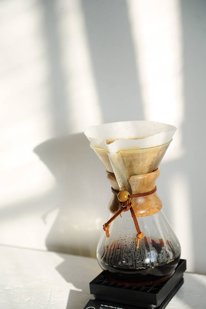 Alternative manual coffee brewing with paper dripper filter. Sun shadows on the white wall - Φωτογραφία, εικόνα