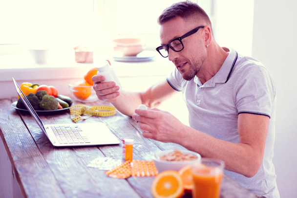Man leading balanced diet holding his morning vitamins having healthy breakfast - Photo, image