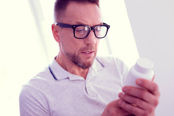 Close up of mature bearded man wearing glasses holding pack of vitamins - Fotó, kép