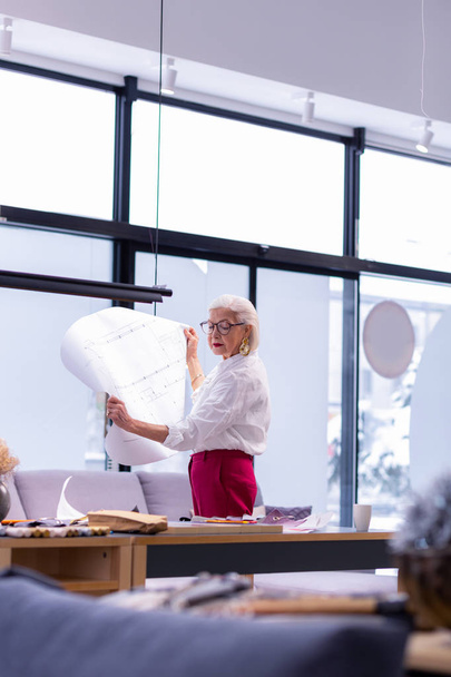 Beautiful aged designer looking concernedly at drawings in her hands - Fotoğraf, Görsel