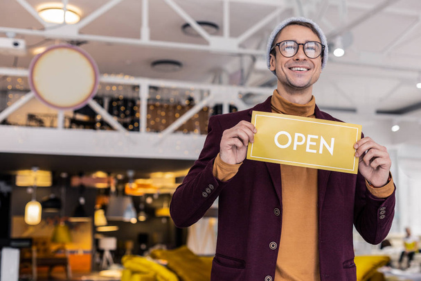Attractive mature beaming brown-haired manager holding open sign in cafe - Foto, Bild