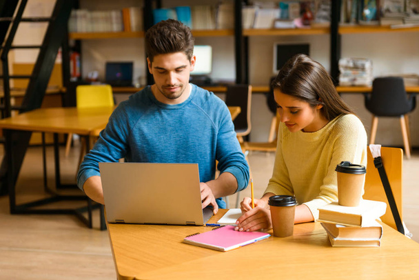 Imagem de um jovem casal de amigos estudantes na biblioteca fazendo lição de casa estudando ler e usar o computador portátil
. - Foto, Imagem
