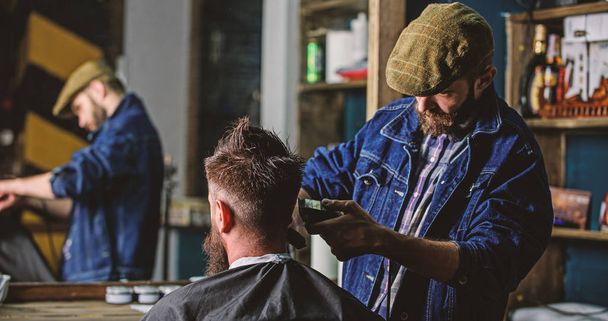 Reflexion of barber with clipper trimming hair of client. Hipster client getting haircut. Hipster lifestyle concept. Barber with hair clipper works on haircut of bearded guy, barbershop background - Φωτογραφία, εικόνα