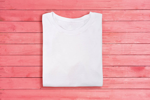 Above view of white folded blank t-shirt on pink wooden background. Female tshirt design template - Fotó, kép