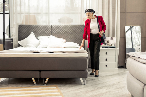 Bewitching fashionable aging woman selecting new grey bed in store - Zdjęcie, obraz
