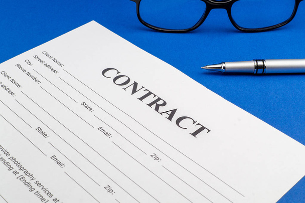 Het contract op de blauwe tafel, bril en pen. - Foto, afbeelding