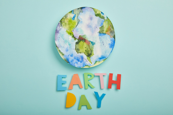 bovenaanzicht van kleurrijke papieren brieven en planeet beeld op een turkooizen achtergrond, aarde dag concept - Foto, afbeelding