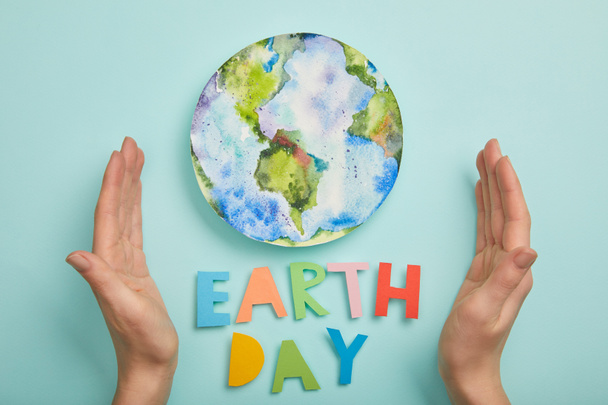 top view of woman holding colorful paper letters and planet picture on turquoise background, earth day concept - Foto, imagen