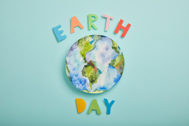Draufsicht auf bunte Papierbuchstaben und Planetenbild auf türkisfarbenem Hintergrund, Earth Day Konzept - Foto, Bild