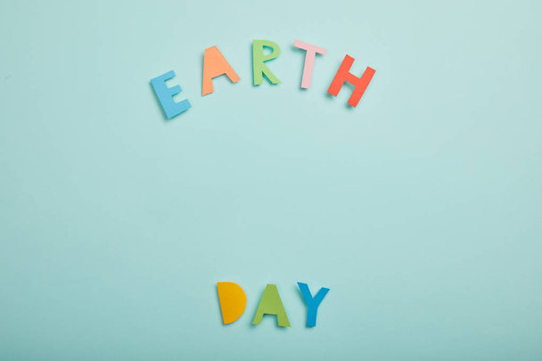 top view of colorful paper letters on turquoise background, earth day concept - Foto, afbeelding