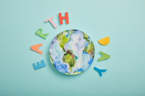 Draufsicht auf bunte Papierbuchstaben und Planetenbild auf türkisfarbenem Hintergrund, Earth Day Konzept - Foto, Bild