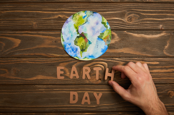 partial view of woman holding paper letters and planet picture on brown wooden background, earth day concept - Foto, immagini