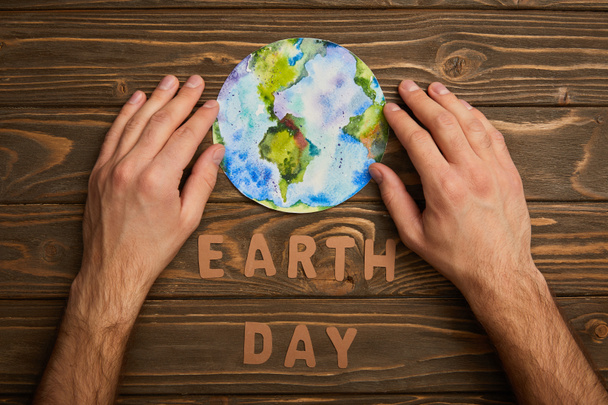 Teilansicht einer Frau mit Planetenbild und Papierbuchstaben auf braunem Holzgrund, Earth Day Konzept - Foto, Bild