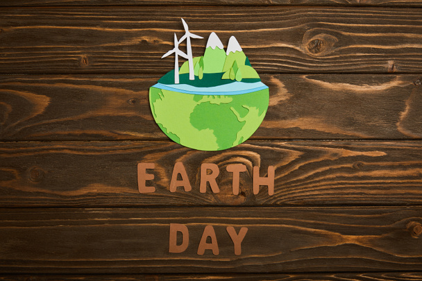 top view of paper cut planet with renewable energy sources and letters on wooden background, earth day concept - Photo, Image