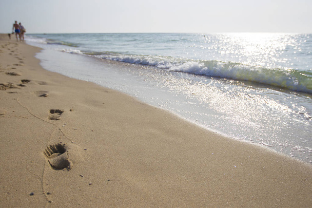 Jalanjälkiä rannalla kävelevien ihmisten hiekassa
 - Valokuva, kuva