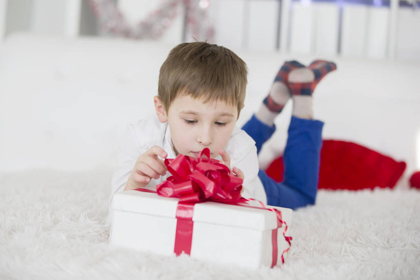 A little boy lying on the bed opens a gift. Get a box with a gift - Фото, изображение