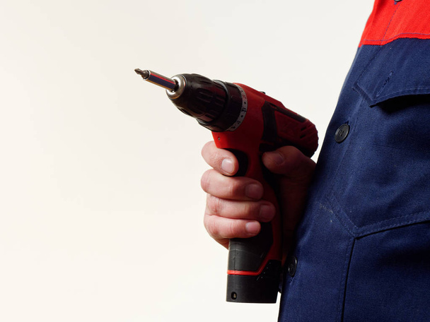 muž v pracovní oděvy obsahuje vrtací nástroj na bílém pozadí - Fotografie, Obrázek