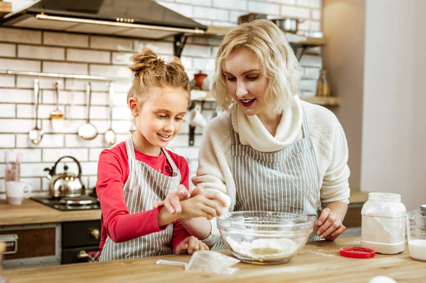 Attentive short-haired mother in apron showing her daughter process of cracking - Foto, Imagem