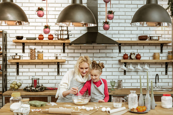Sonriente señora rubia sentada con su hija en la elegante cocina llena
 - Foto, Imagen
