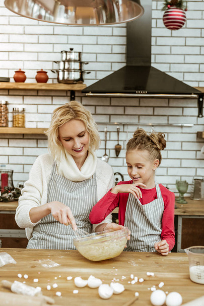 Cooking smiling mother and her curious daughter having mess on cooking table - Фото, изображение