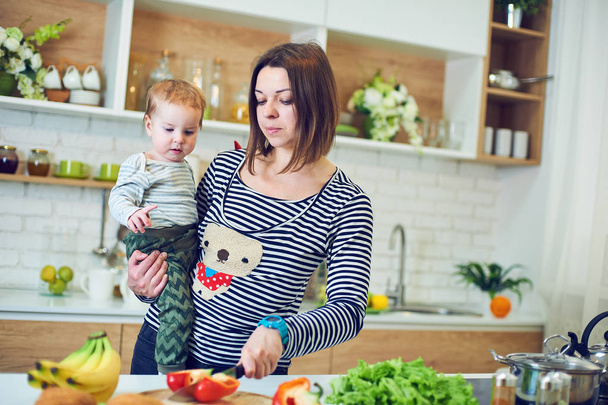 Mujer joven y feliz sosteniendo a un niño de 1 año y cocinando juntos en la cocina
 - Foto, imagen