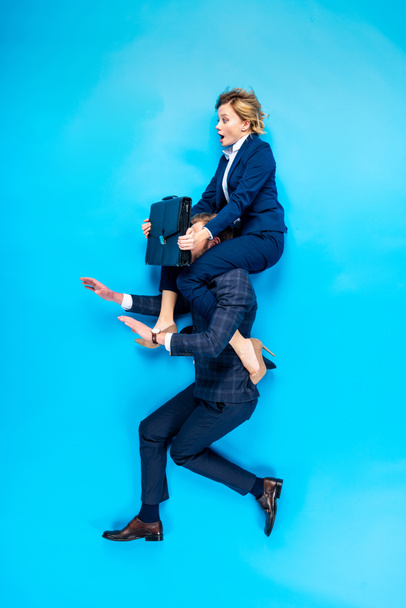 Man holding on shoulders shocked woman with briefcase on blue background - Foto, afbeelding