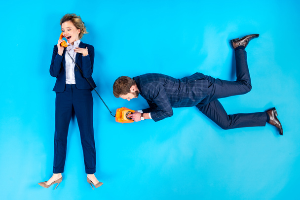 Man dialing number while woman talking on telephone on blue background - Foto, Imagem