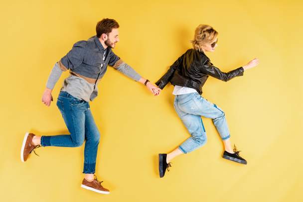 Fashionable couple holding hands and running on yellow background - Foto, Bild