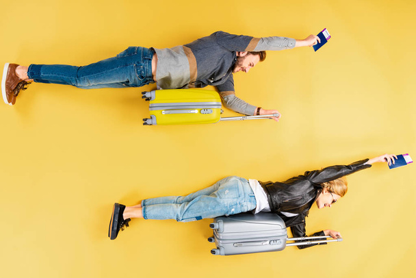 Funny couple lying on suitcases and holding tickets on yellow background - Photo, Image