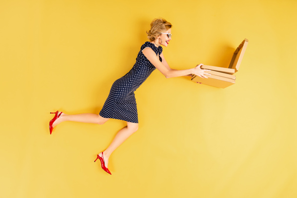 Smiling woman in elegant dress holding pizza on yellow background - Foto, imagen