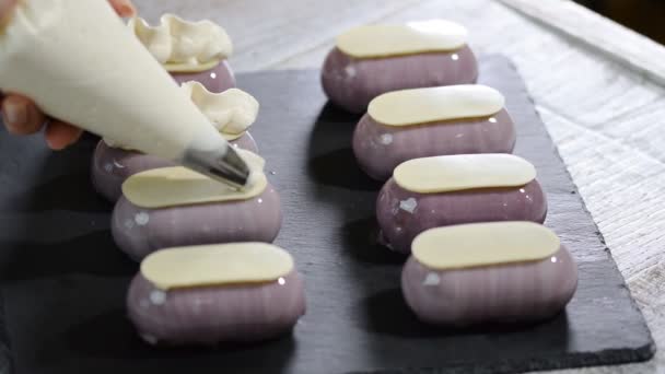 Banketbakker versieren kleine cakes met slagroom op keuken. - Video