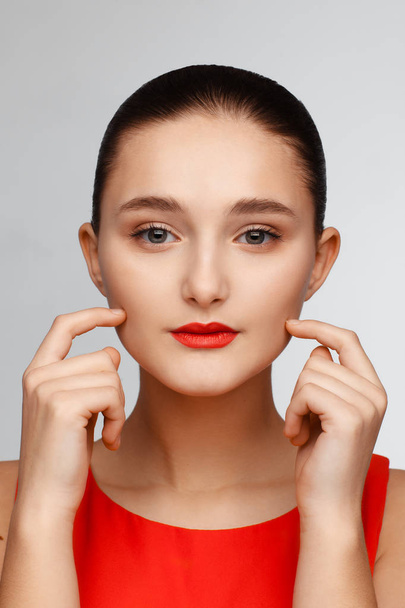 Portrait of a beautiful young girl with red lips and in a red blouse. Gray background - Photo, image