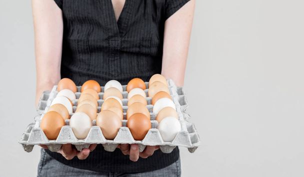 Donna caucasica con camicia nera con una scatola di uova di cartone piena di uova di gallina
. - Foto, immagini