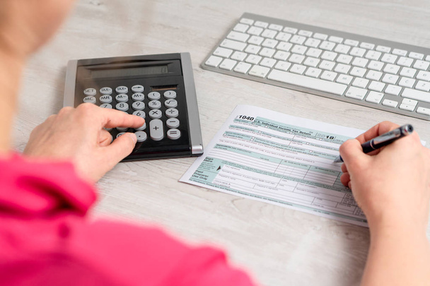 Sur la photo de l'épaule de la femme calculant et remplissant le formulaire d'impôt américain à côté du clavier d'ordinateur et le formulaire d'impôt 1040. 15 avril 2019 jour d'imposition
 - Photo, image