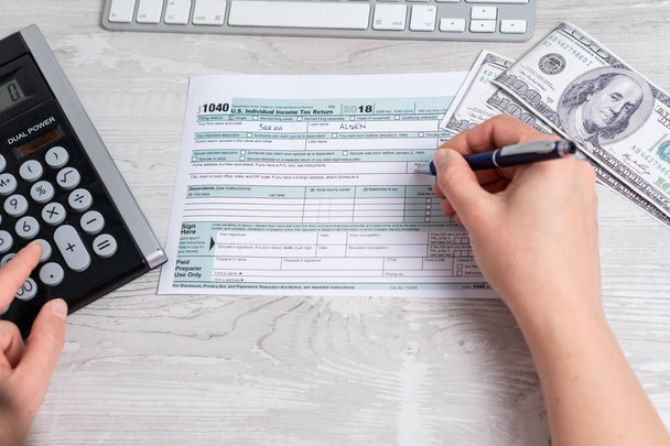 Point of view photo of woman calculating and filling US tax form next to computer keyboard, dollar bills and tax form 1040. 15th April 2019 tax day - Photo, Image