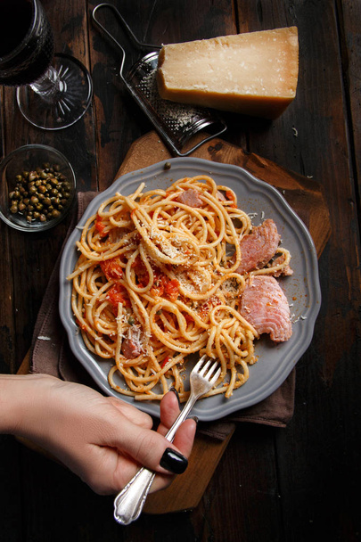 Spaghetti with chunks of fresh tuna, tomato and capers on a dark background - 写真・画像