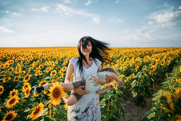 Mom and son are playing in the field of sunflowers at sunset - Photo, Image