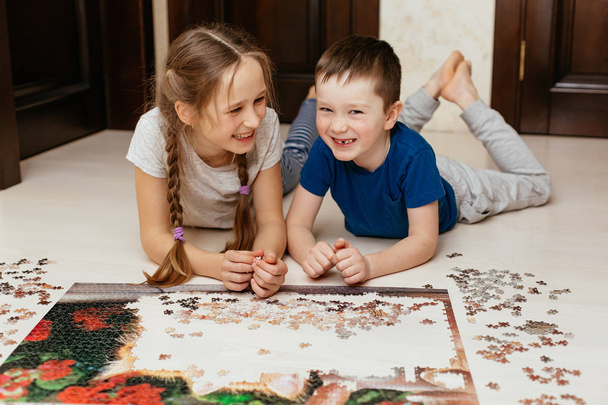 Girl and boy collect puzzle on the floor in the house - Photo, image