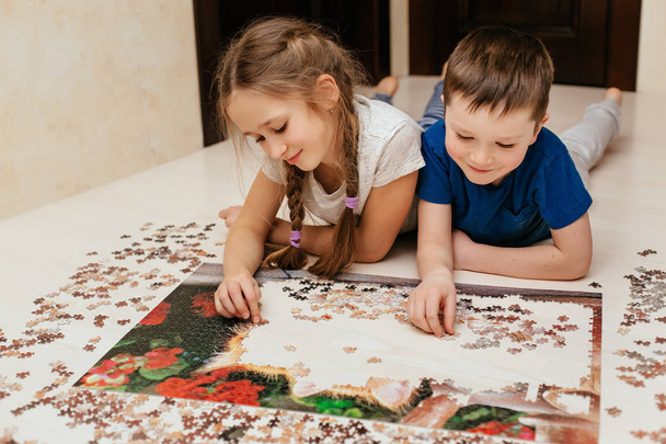 Girl and boy collect puzzle on the floor in the house - Photo, image