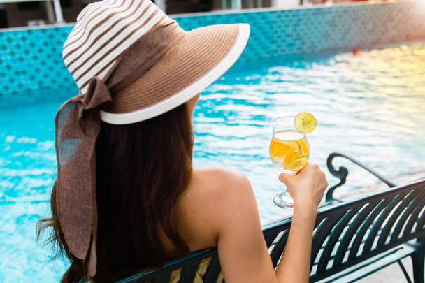 chica sentarse al lado de piscina swimmimg mano celebración de jugo de naranja por la mañana
 - Foto, Imagen