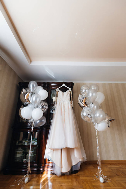 Hääpuku roikkuu kaapissa ja puhallettavat pallot lähellä valkoista mekkoa
 - Valokuva, kuva