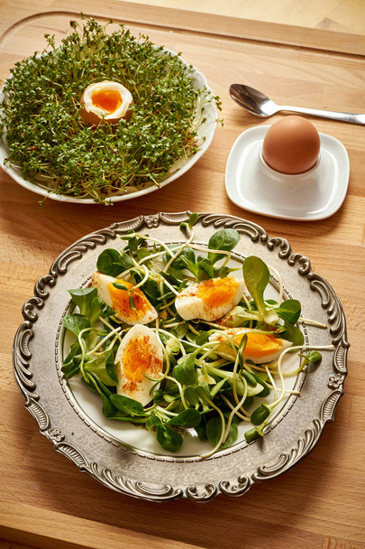 Vintage plate with spring breakfast with sprouts and lambs lettuce and boiled eggs and cress on wooden table - Photo, Image