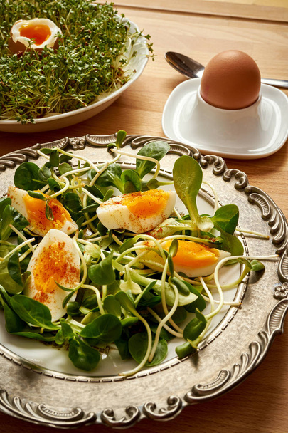 Vintage πλάκα με πρωινό την άνοιξη με ηλιέλαιο λάχανα και αρνιά, μαρούλι και αυγά βραστά και Κάρδαμο στο φωτεινό ξύλινο τραπέζι - Φωτογραφία, εικόνα