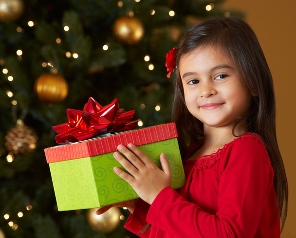 Girl Holding Christmas Present In Front Of Tree - Foto, Imagen