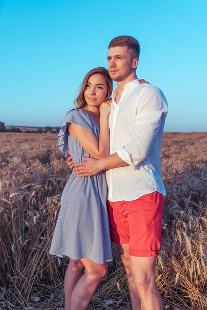Beautiful and young couple, man and a woman meet the sunset and dawn in the summer in a wheat field. Concept of love caring, hugging family happiness and support. - Photo, image