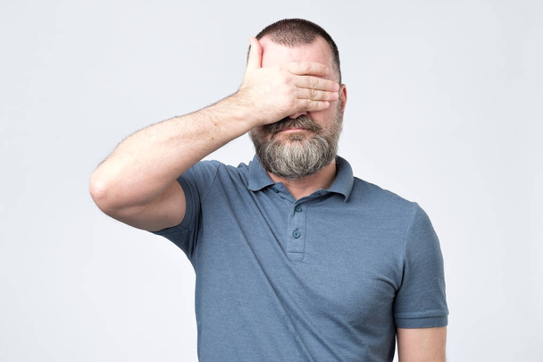Homme en t-shirt bleu couvrant son visage avec des mains
 - Photo, image