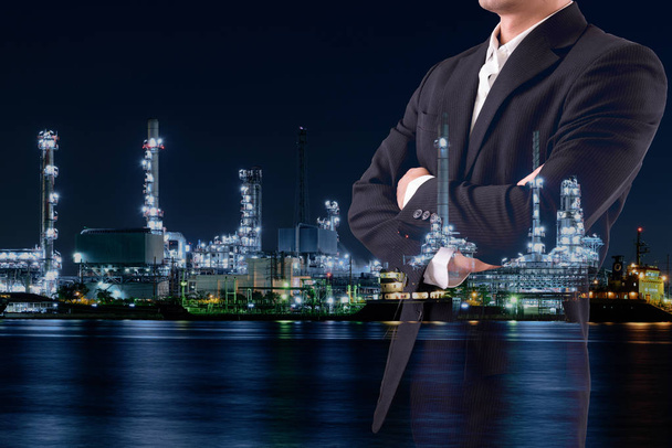 Üzleti koncepció vagy energia menedzsment: dupla expozíció üzletember kopás fekete öltöny tartás fegyverek átlépte a háttérben az olajfinomítók - Fotó, kép