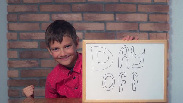παιδί κάθεται στο γραφείο κρατώντας πινακάκι με γράμματα ημέρα o - Φωτογραφία, εικόνα